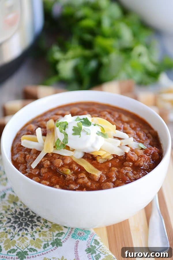 Instant Pot Lentil Chili Stovetop and Slow Cooker Variations 5 A white bowl full of lentil beef chili topped with sour cream and cheddar cheese.