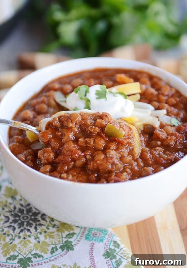 Instant Pot Lentil Chili Stovetop and Slow Cooker Variations 6 A spoon taking a bite out of a white bowl full of lentil and beef chili.