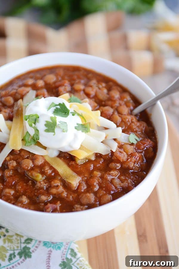 Instant Pot Lentil Chili Stovetop and Slow Cooker Variations 7 A white bowl of lentil chili topped with sour cream, cheddar cheese, and parsley.