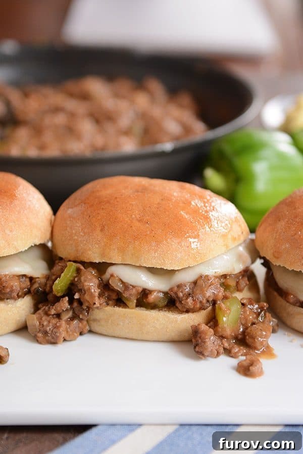 A philly cheesesteak sloppy joe on a golden brown bun, with some of the mixture spilling out onto the plate.