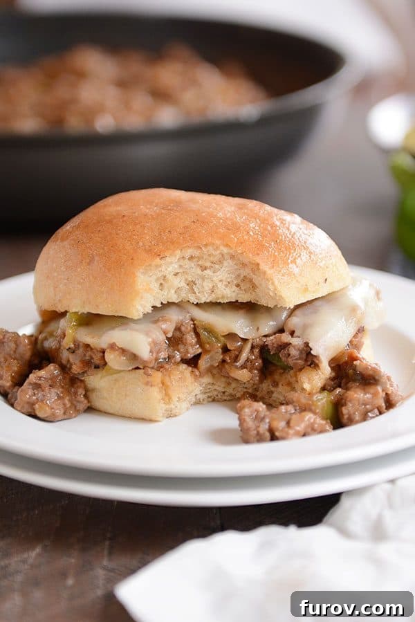 A white plate with a philly cheesesteak sloppy joe with a bite taken out.