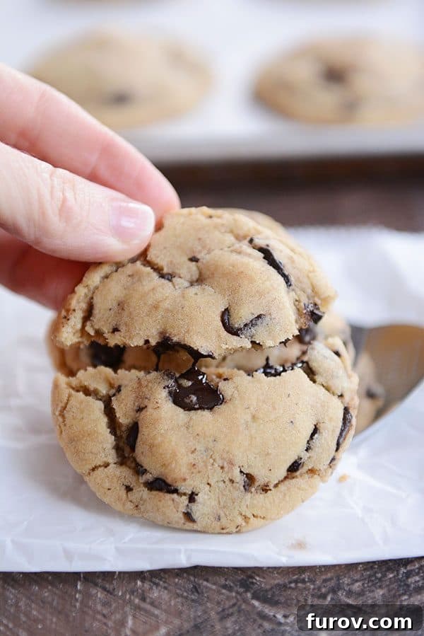A thick and gooey chocolate chip cookie getting split in half, revealing melted chocolate inside. 