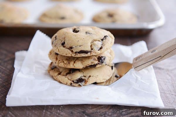 Three golden brown chocolate chip cookies stacked on a metal spatula, ready to be served.