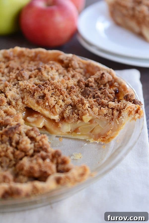 No-Fuss Apple Crumble Pie 3 A stunning full apple crumble pie in a glass pie dish, with one perfect slice carefully removed, revealing the sweet, baked apple filling and golden streusel.