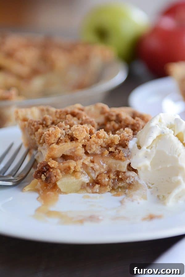 No-Fuss Apple Crumble Pie 5 A close-up of a slice of apple crumble pie with a bite taken out, sitting next to a melting scoop of vanilla ice cream on a white plate, highlighting the delicious texture contrast.