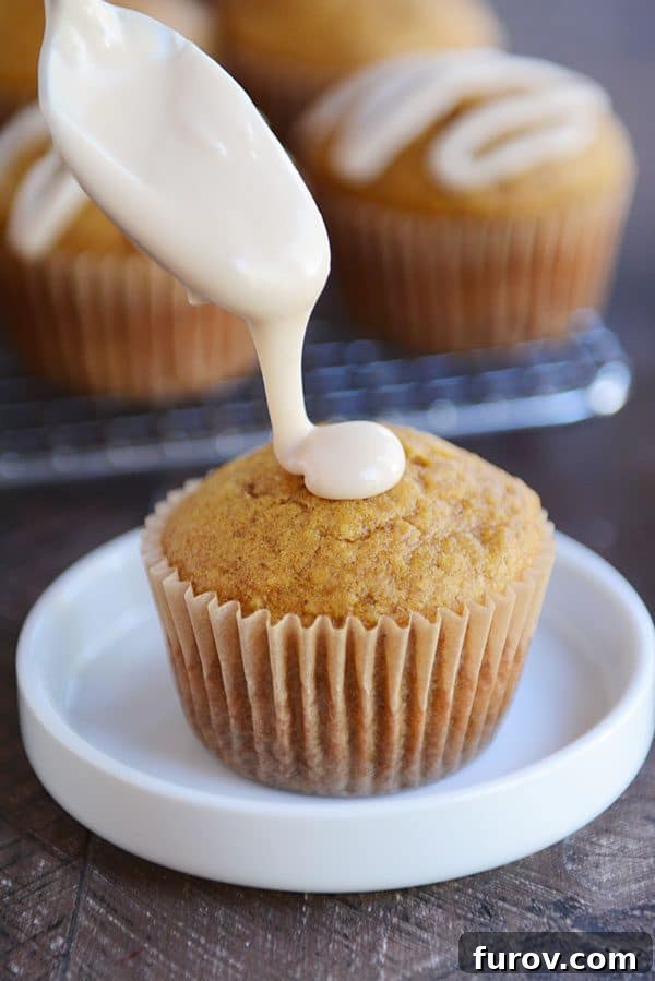 A stream of rich, white maple frosting elegantly flowing onto a pumpkin muffin, highlighting its soft texture.