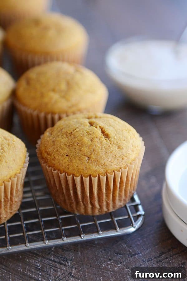 Freshly baked pumpkin muffins cooling on a wire rack, next to a bowl of creamy frosting.