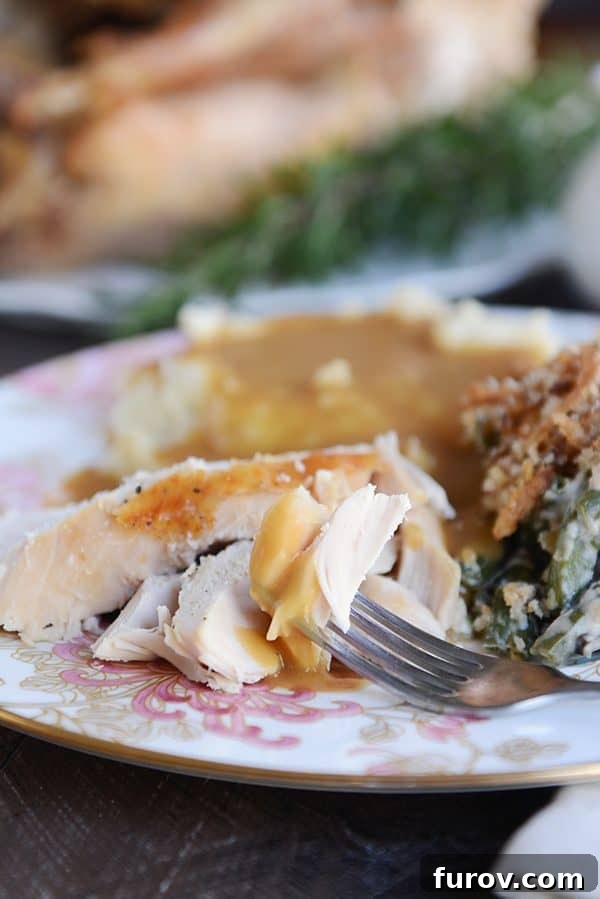 Juicy & Golden Thanksgiving Turkey in an Oven Roasting Bag 4 A fork lifting a bite of turkey covered with rich brown gravy from a white plate.