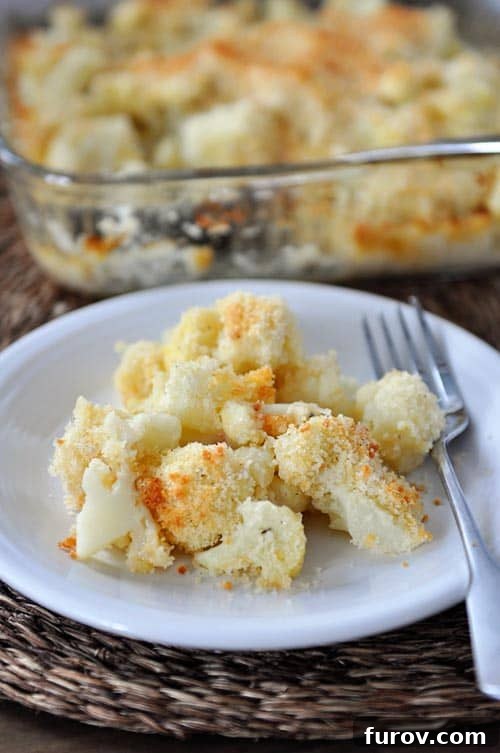 Ultimate Cheesy Cauliflower Bake 2 A white plate showcasing a generous serving of baked cheesy cauliflower with a fork resting beside it, ready to be enjoyed.