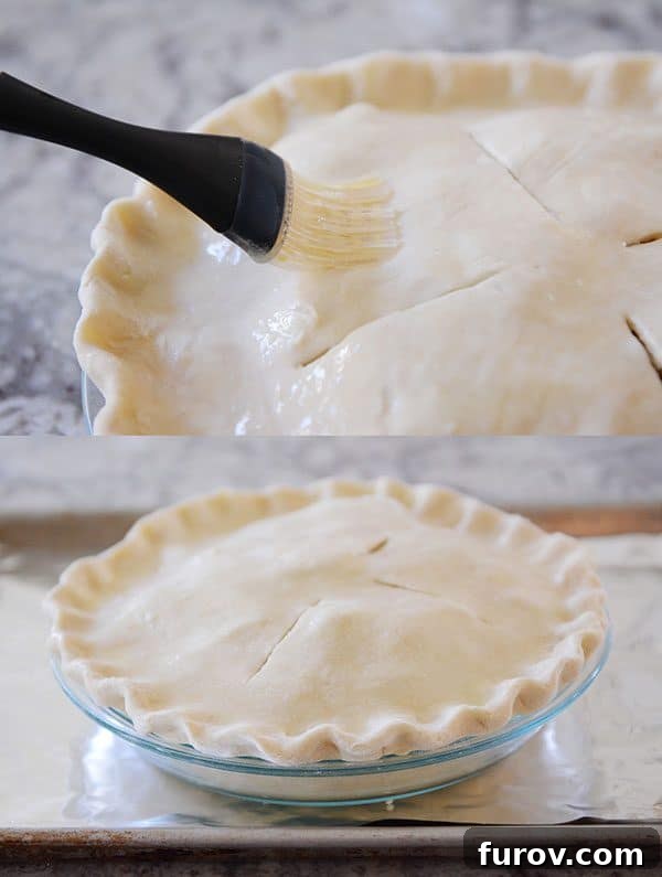 An uncooked pie crust being brushed with an egg wash, ready for baking to achieve a golden, glossy finish.