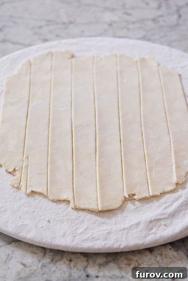 Unbaked pie crust meticulously cut into uniform strips, ready for weaving into a lattice design.