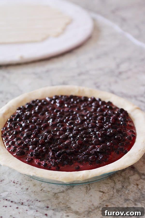 An uncooked pie generously filled with a vibrant berry mix, awaiting its lattice top.