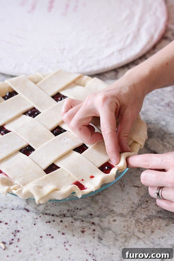 An uncooked lattice pie crust receiving its final crimped edges, showcasing a homemade artisan touch.