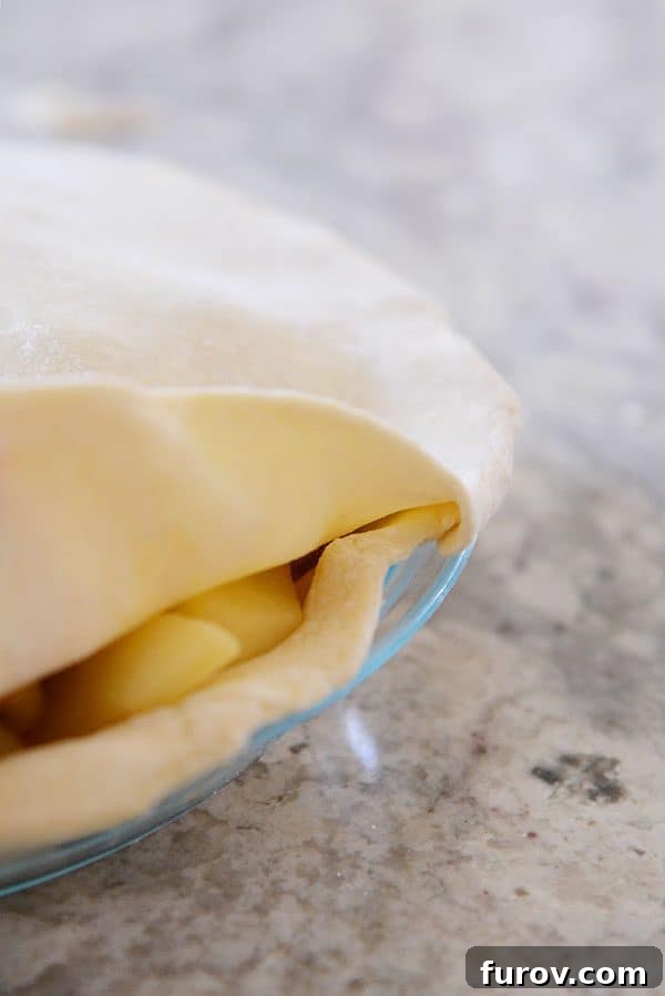 An apple pie undergoing the critical step of folding the top pie crust underneath the bottom crust to create a strong seal.