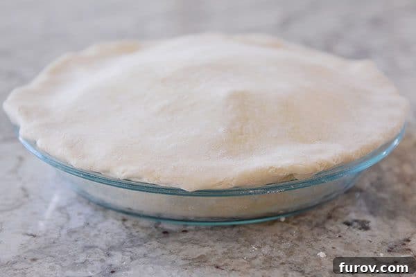 An uncooked double crust pie, perfectly sealed and ready for fluting, showcasing the tucked-under top crust.