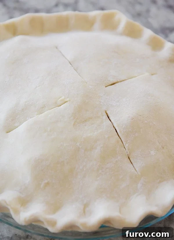 Top-down view of an uncooked full-crust pie with four strategically placed slits to allow steam to escape during baking.