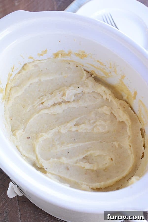 Hands-Off Creamy Slow Cooker Mashed Potatoes 2 A white crockpot full of creamy mashed potatoes, ready to be served.