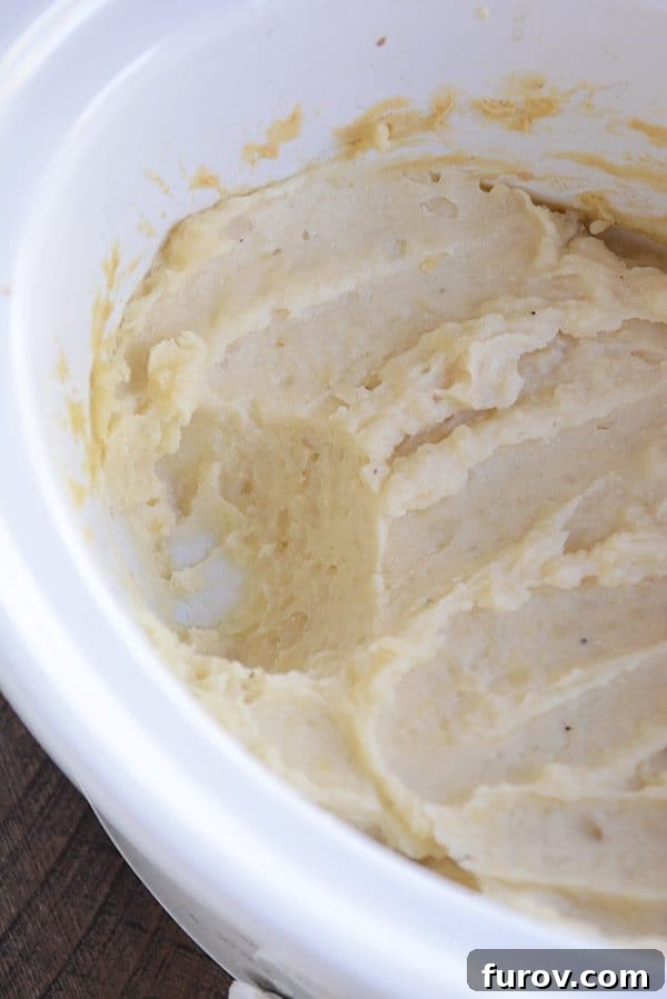 Hands-Off Creamy Slow Cooker Mashed Potatoes 4 A white crockpot full of unmashed, tender potatoes after slow cooking.