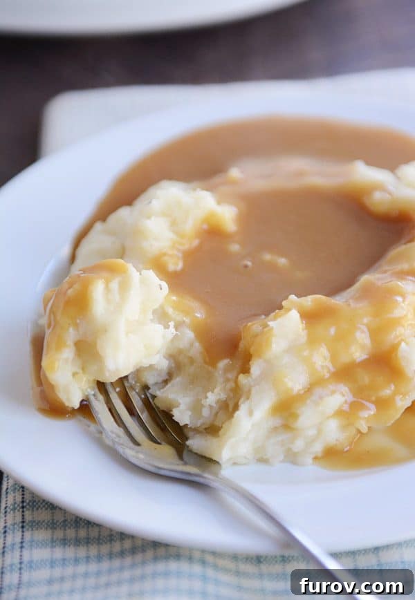 Hands-Off Creamy Slow Cooker Mashed Potatoes 5 Close-up of mashed potatoes covered in brown gravy on a white plate, highlighting their creamy texture.