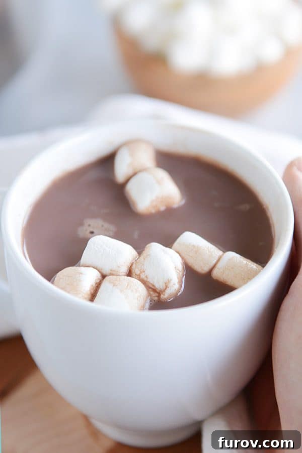 A white mug of steaming hot chocolate and marshmallows floating on the top.