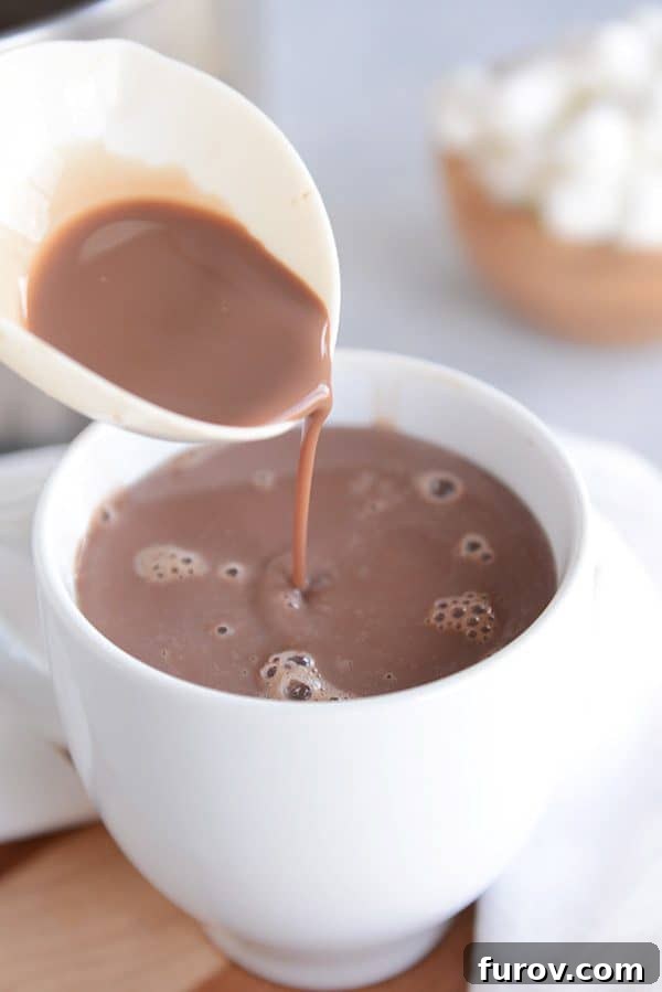 A ladle of hot chocolate being poured in a white mug. 