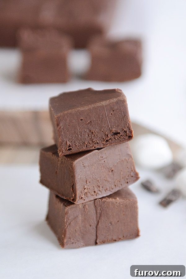 Three cubes of fudge stacked on top of each other, with more cubes in the background. 