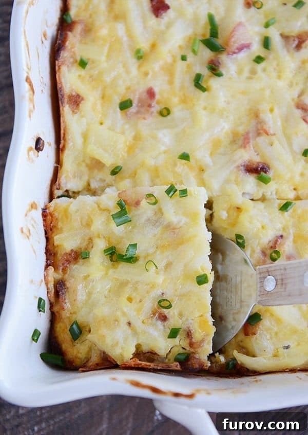 A dish full of cheesy egg casserole sprinkled with green onion. The front left piece is cut and being scooped out.