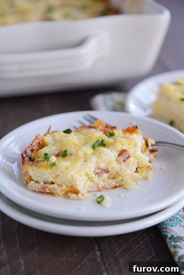 A piece of cheesy egg and hash brown casserole on a white plate, with a bite taken out.