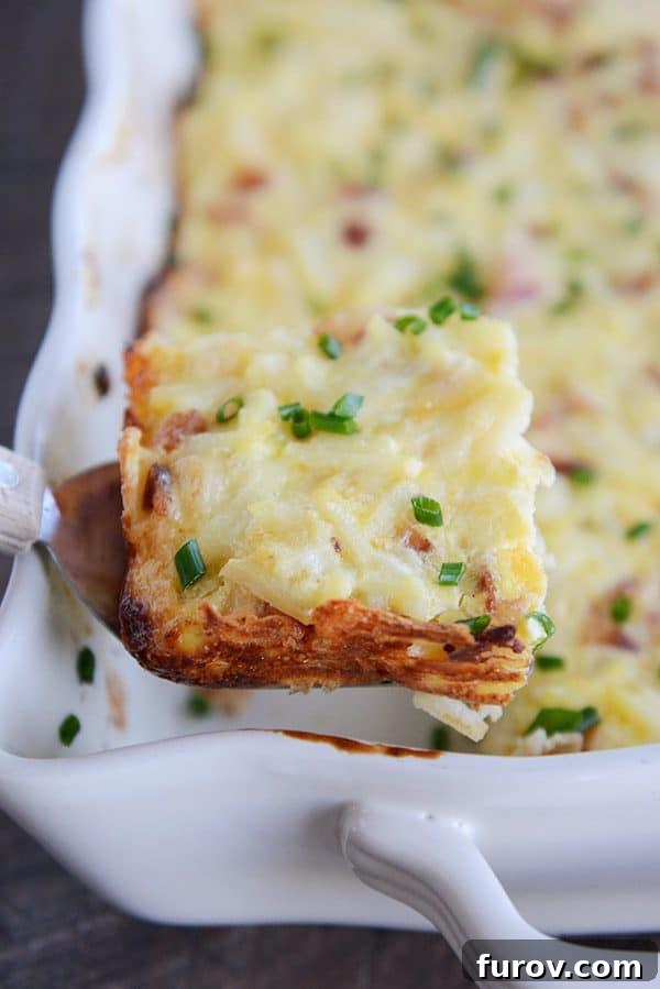 A dish full of cheesy egg casserole sprinkled with green onion. The front left piece is cut and being scooped out.