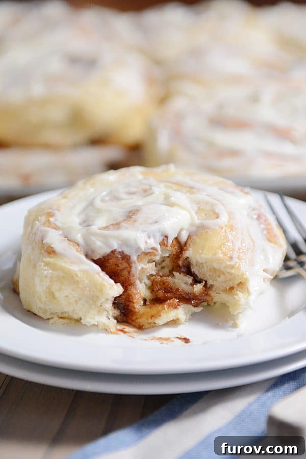 A frosted cinnamon roll with a bite taken out, revealing the perfectly swirled cinnamon filling and incredibly soft interior.