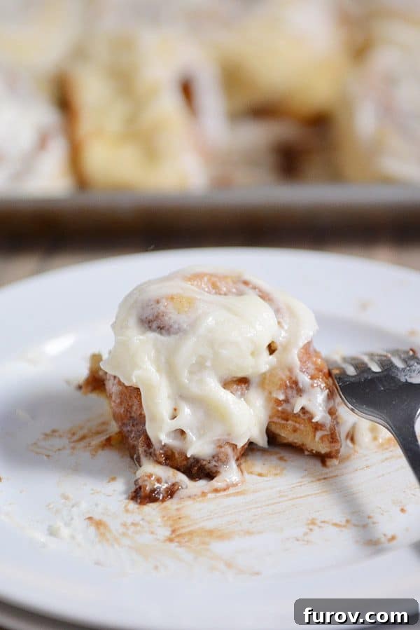A partially eaten cinnamon roll on a white plate, showing the rich, gooey filling, distinct layers, and smooth, abundant icing.