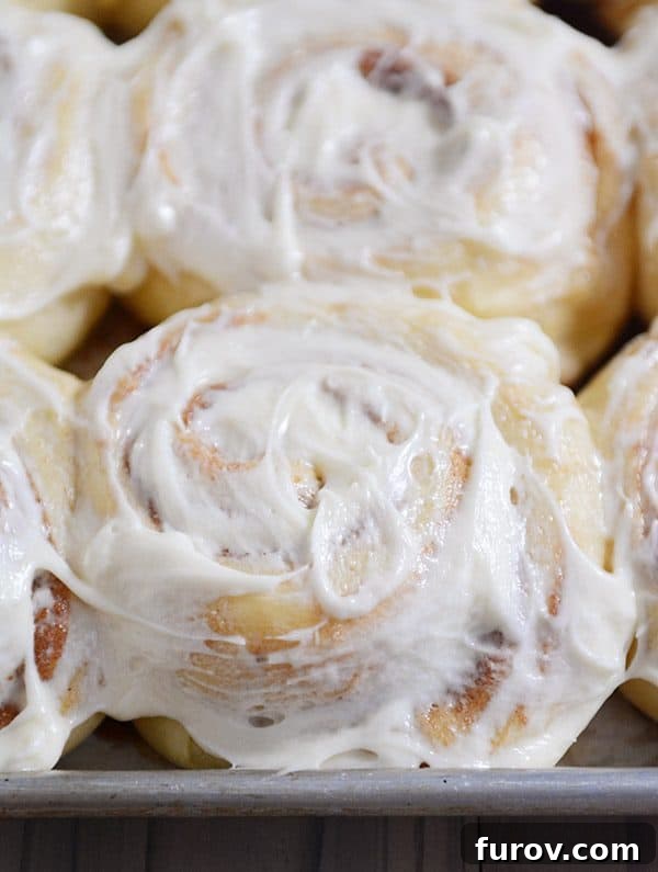 Top view of a pan of frosted cinnamon rolls, glistening with creamy, smooth icing, meticulously arranged and ready to be served.