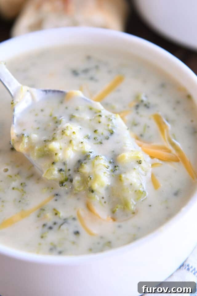 Spoon scooping bite of broccoli cheese soup in white bowl.
