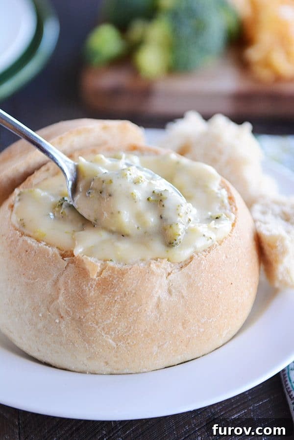 Spoon dipping into bread bowl filled with broccoli cheese soup.
