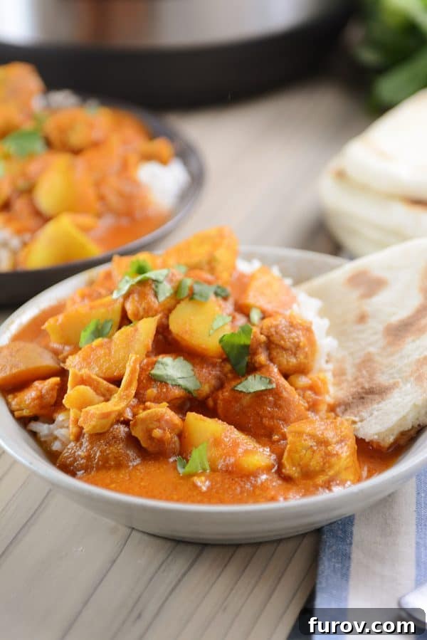 A bowl of white rice topped with Indian butter chicken and potato curry, garnished with fresh cilantro.
