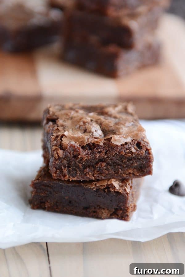 Two chocolate brownies stacked on top of each other on a piece of parchment paper. 