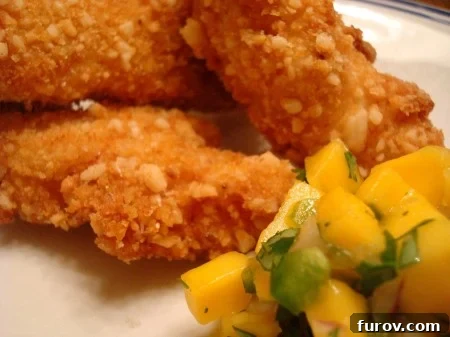 Island Macadamia Chicken with Zesty Mango Salsa 2 Golden brown macadamia-crusted chicken served with a vibrant mango salsa on a white plate, garnished with fresh cilantro.