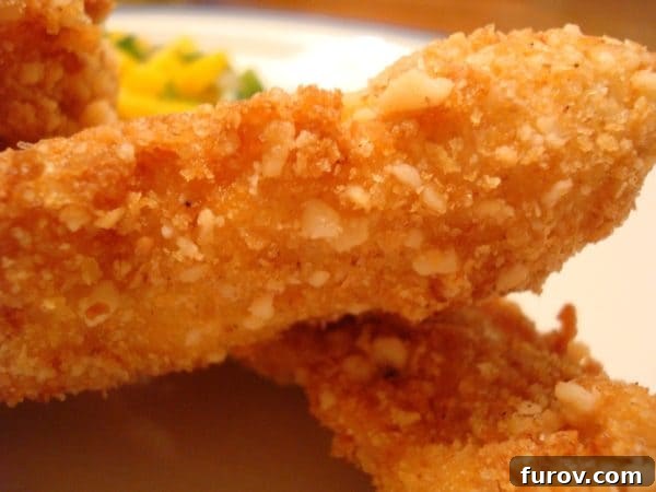 Island Macadamia Chicken with Zesty Mango Salsa 3 Two perfectly fried macadamia-crusted chicken strips on a simple white plate, ready to be served.