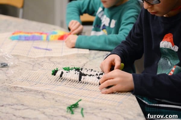 A child's hand working on a latch hook kit with colorful yarn.