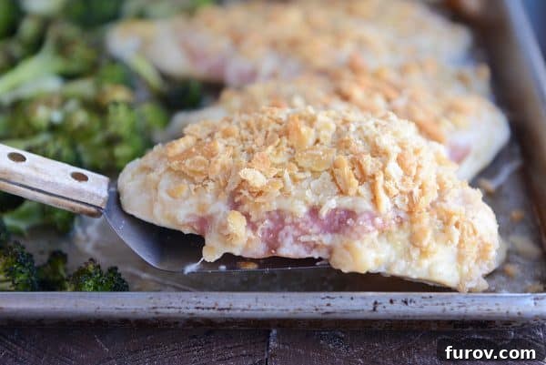 One-Pan Cordon Bleu Chicken & Broccoli Roast 4 A spatula lifting a piece of golden brown unstuffed sheet pan chicken cordon bleu from a baking sheet, showcasing its crispy topping.