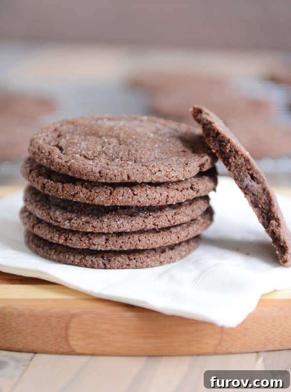 A stack of soft chocolate sugar cookies on a white napkin, with one broken in half to show the soft interior.