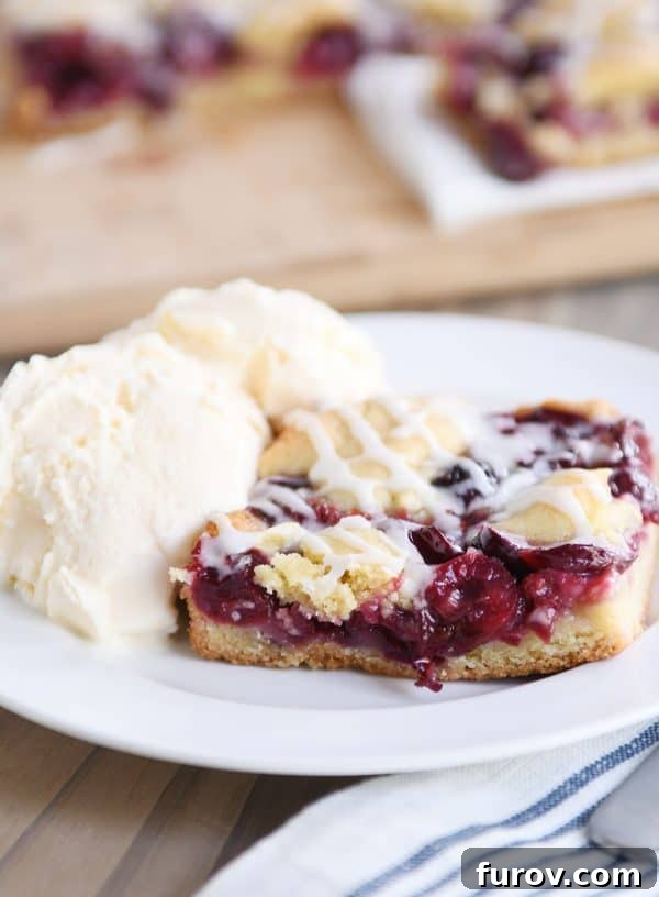 A large piece of cherry pie cookie bar next to a scoop of vanilla ice cream, ready to be enjoyed.