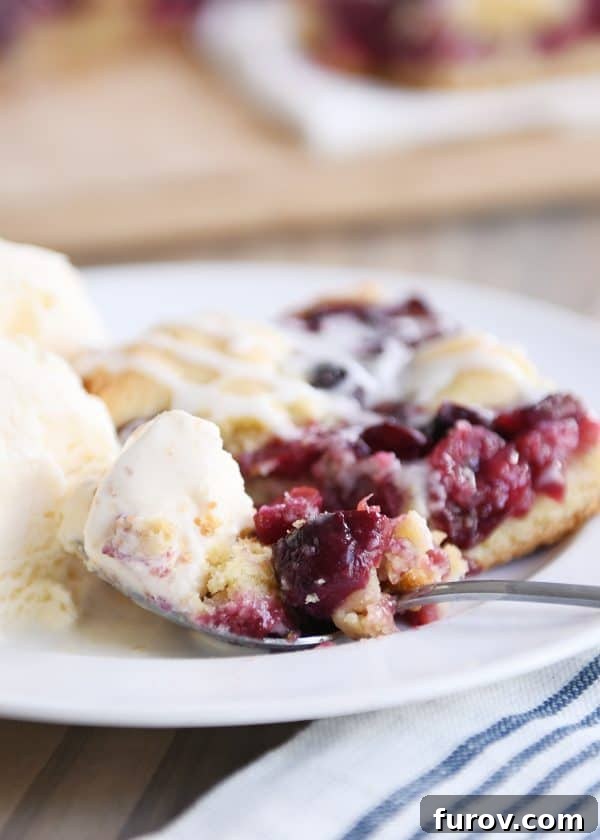 Cherry pie cookie bar on a white plate with a scoop of ice cream, beautifully presented.