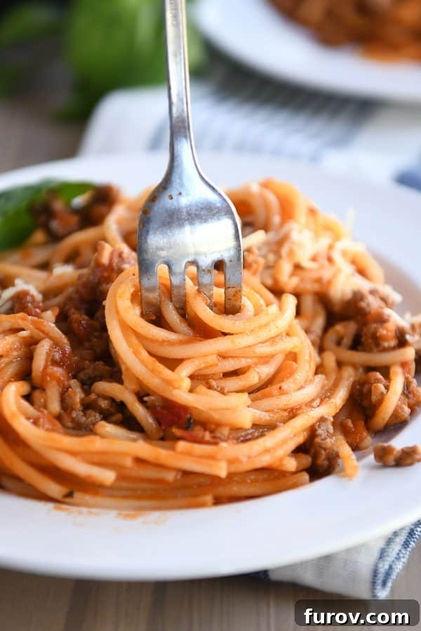 Twisted Instant Pot spaghetti with meat sauce on a white plate, garnished with fresh basil.