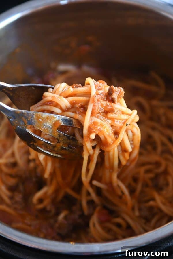 Tongs lifting perfectly cooked Instant Pot spaghetti out of the pressure cooker.