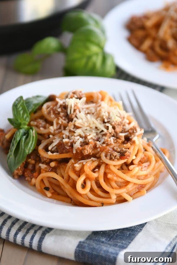 Instant Pot spaghetti on a white plate, garnished with fresh basil leaves.