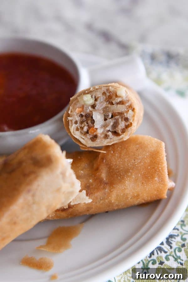 Marys Signature Egg Rolls 3 A perfectly fried egg roll, cut in half to reveal its flavorful filling of meat, noodles, and vegetables, resting on a clean white plate.