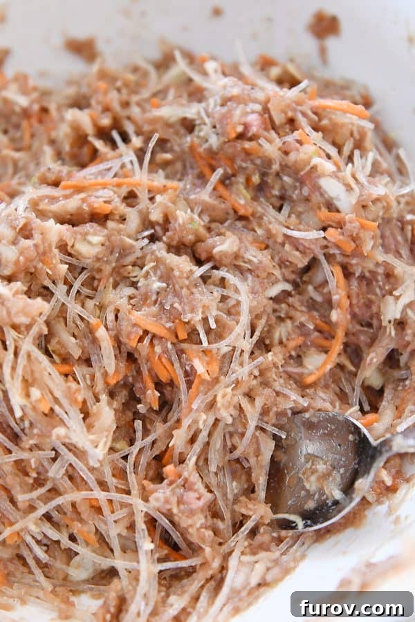 Marys Signature Egg Rolls 5 A large white bowl filled with the prepared egg roll mixture, featuring ground meat, shredded vegetables, and noodles, perfectly combined and ready for wrapping.