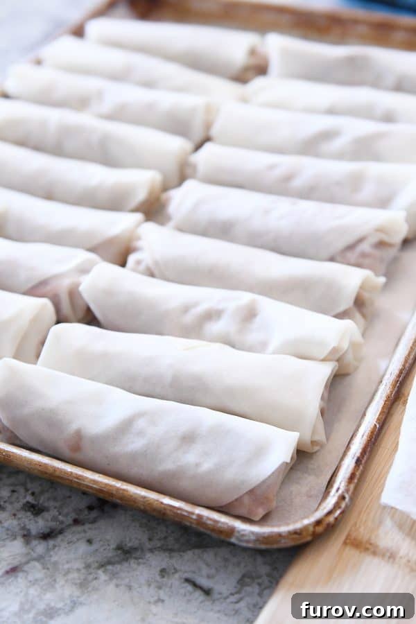 Marys Signature Egg Rolls 7 A full cookie sheet neatly arranged with uncooked egg rolls, resting on parchment paper, awaiting their turn in the hot oil for frying.