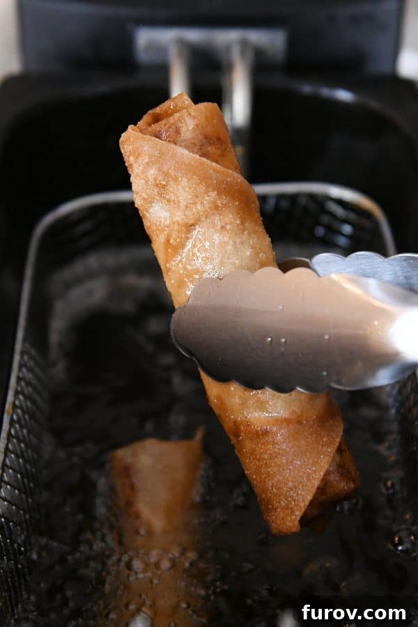 Marys Signature Egg Rolls 8 A golden-brown, crispy egg roll being carefully lifted out of a deep fryer with tongs, ready to be drained and served.
